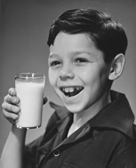 Boy (8-9) holding glass of milk, smiling (B&W), portrait