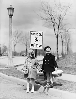 Sidewalk Prints: Boy and girl walking to school, about cross street by slow school sign