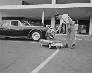 Prints of 1961, Two People, Child, Boys, Mid Adult, Mid Adult Men, Caucasian Appearance, Horizontal, Black And White, Photography, Three Quarter Length, Full Length, Uniform, Bending, Sitting, Holding, Giving Tom Kelley Archive Prints: Boy sitting in toy car giving paper to traffic police officer
