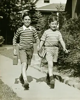 10 11 Years Prints: Two boys (10-11) walking side by side in suburbs, carrying books, (B&W)