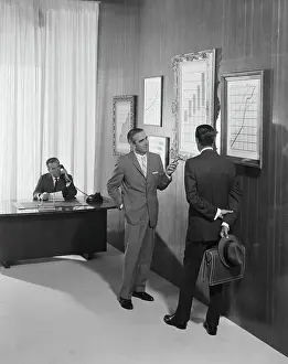 Only Mature Men Prints: Two businessman discussing at bar chart while another man using telephone in background