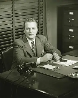Stationery Prints: Businessman holding pencil, sitting at office, (B&W)