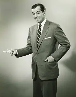 Hand In Pocket Prints: Businessman pointing sideways in studio, smiling, (B&W), portrait