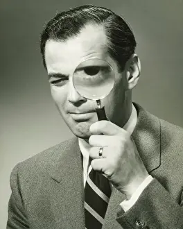30 35 Years Prints: Businessman in full suit in studio looking through magnifying glass, (B&W), portrait