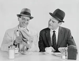 Fedora Prints: Two businessmen in suits and fedoras having breakfast at diner, looking at newspaper