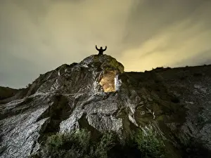 Cave excavated in the rock, on the top of a mountain with a man raises with the arms raised in the night