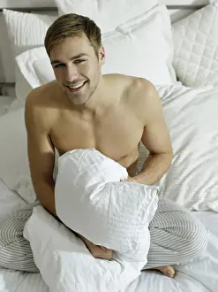 Merry Prints: Charming bare chested man wearing pyjamas sitting on a bed, smiling