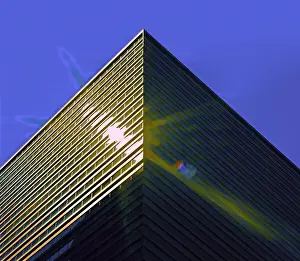 A color photograph of the sun reflected off the corner of a commercial skyscraper in downtown Seattle, Washington with a resulting lens flare. This photo was taken on June 20, 2021