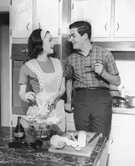 Couple standing in kitchen, smiling, (B&W)