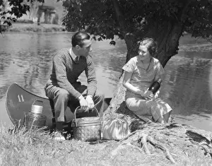 Plaid Prints: Couple Young Man Woman Smiling In Front Of Canoe With Picnic Basket Thermos Man Sweater