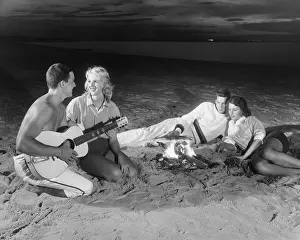Two couples on beach sitting around campfire