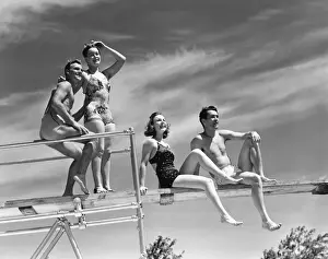 Two couples sitting on springboard, (B&W), low angle view
