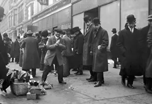 A crowd on a sidewalk observes street peddlers selling toys
