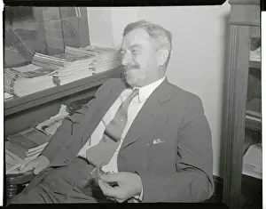 Earl Browder Leaning Back in Chair and Holding Eyeglasses