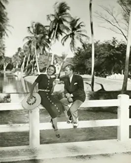 Elegant couple sitting on fence in tropical environment, (B&W)