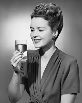 Raising Prints: Elegant woman holding glass of water in studio, (B&W), portrait