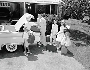 Family packing suitcases in trunk of car parked on driveway, preparing for vacation