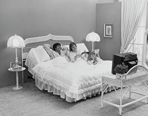 Mid Adult Collection: Father and mother with daughter lying on bed watching tv, smiling