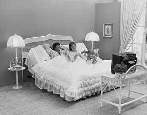 Casual Collection: Father and mother with daughter lying on bed watching tv, smiling