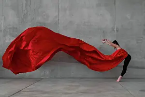 Prints of Female ballet dancer on pointes dancing with a large red veil in front of a grey concrete wall The Enchanting Evolution of Ballet: Female ballet dancer on pointes dancing with a large red veil in front of a grey concrete wall