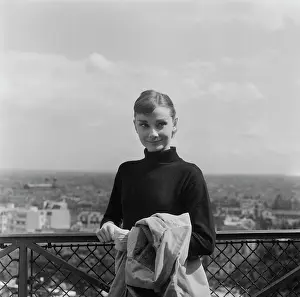 Prints of British actress Audrey Hepburn (1929-1993), her raincoat over her arm as she poses in a black turtleneck sweater during a break in filming Funny Face in Paris, France, July 1956 Elegance Personified – A Classic Art Print Collection: Filming Funny Face, 1956