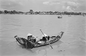 Prints of Two people wearing traditional Vietnamese non la hats on a sampan with fishing nets on a stretch of the Saigon River as it flows through Saigon, Vietnam, 30th August 1965 Vietnam Prints: Fishing On The Saigon River