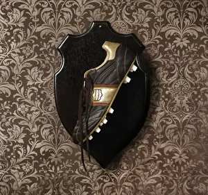 Prints of Decorative wall paper with a soccer shoe hanging as a trophy on a wooden plaque Stone Prints: Football boot hanging as a trophy on a wall