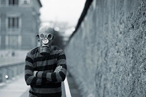 Gas Mask Man stands next to the Berlin Wall