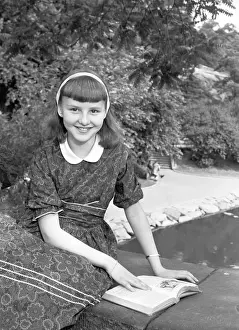 Girl (12-13) sitting on wall with book, (B&W), portrait