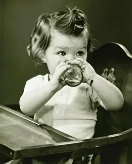 Preschooler Prints: Girl (2-3) sitting in high chair, drinking water from glass, (B&W)