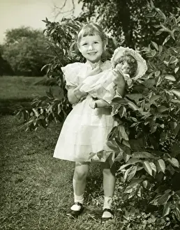 Girl (6-7) holding doll, posing in park, (B&W), (Portrait)