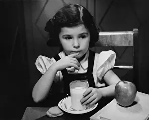 Girl (6-7) sitting at table, having breakfast, (B&W)