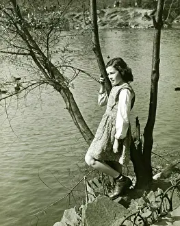 Only Girls Prints: Girl (8-9) leaning on tree trunk by water, (B&W), elevated view