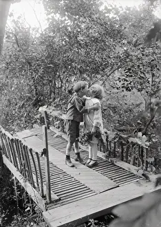 Baby Girl Prints: Girl and boy (6-7 years) kissing on bridge. August 05, 1925