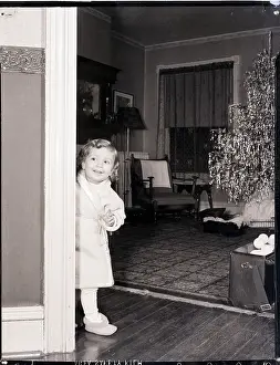 Prints of (Original Caption). A young girl wearing a robe and slippers enters the family room at Christmas time. A tree decorated with icicles stands in the background. Undated photograph A Timeless Christmas: Vintage Treasures: Girl and Christmas Tree