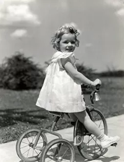 Girl wearing summer dress, riding tricycle down sidewalk. (Photo by H. Armstrong Roberts / Retrofile / Getty Images)