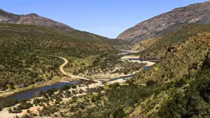 Open Space Prints: A gravel road in a mountainous area crossing over a river on a low level bridge near