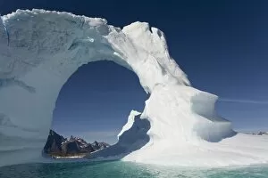 Greenland, Frederiksdal, Arched iceberg frames mountain peaks on Pamiagdluk Island