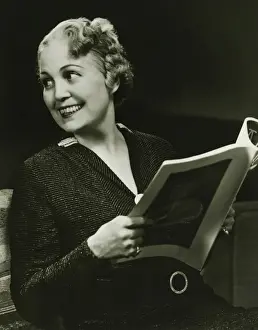 50 59 Years Prints: Well groomed mature woman holding fashion magazine in living room, (B&W), portrait