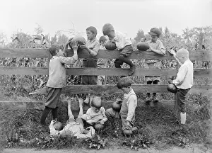 Quality Time Prints: Group of children (4-12 years) by fence, holding pumpkins. August 05, 1925