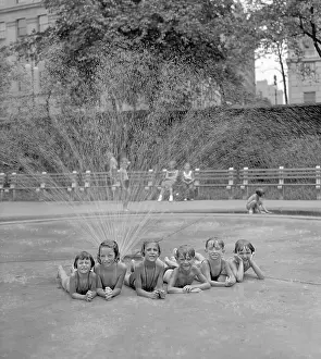 Group of girls (6-7) and (8-9) boys taking refuge from heat under sprinkler