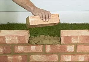 Hand holding brick above mortar between gap in wall, close up