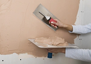 Holding a plastering hawk and spreading plaster onto a wall with a trowel Holding a plastering hawk and spreading plaster onto a wall with a trowel