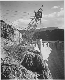 Prints of A black and white photograph of a transmission line tower and a portion of the Hoover Dam, the tower was built on a cliff face and stands angled out over the canyon A Timeless Collection of Hoover Dam Photography: Hoover Dam Transmission Lines