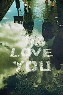 Street Art Collection: I LOVE YOU stencilled on street with rain puddle reflecting sky and passers by