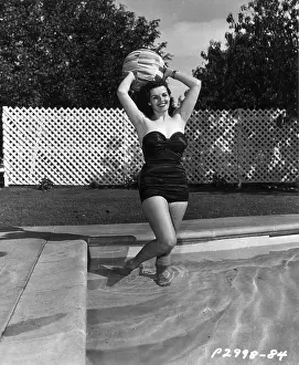 Prints of 1951: Full-length portrait of American actor Jane Russell, wearing a strapless one-piece swimsuit, holding a beach ball over her head while standing in a swimming pool Hollywood's Sultry Siren – A Photographic Tribute: Jane Russell