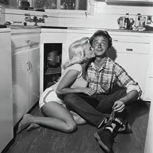 Prints of American actress and singer Jayne Mansfield (1933-1967) kisses American actor Lance Fuller (1928-2001) on the cheek as sits on the floor with his back against a cupboard, in an domestic setting Hollywood's Blonde Bombshell in Focus: Lance Fuller & Jayne Mansfield