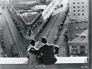 Prints of Comedy team Laurel and Hardy sitting atop building scaffolding, look down on city street in film scene from the 1920s Timeless Comedy Icons: Classic Moments from the Legendary Duo: Laurel and Hardy Atop Building