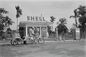 Prints of A motorcycle rickshaw driver, wearing a safari-style hat, stops for petrol at a Shell Station in Saigon, Vietnam, 30th August 1965 Vietnam Prints: Life In Saigon