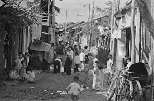 Prints of Vietnamese women and children on a rundown street, with a makeshift shelter against a building on one side, and bicycles against buildings on the opposite side, in Saigon, Vietnam, 30th August 1965 Vietnam Prints: Life In Saigon